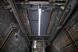 View from inside an elevator shaft showing exposed brick walls, metal rails, cables, and a fluorescent light fixture on the ceiling—highlighting the robust design found across various industries served.