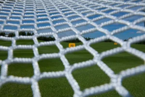 Close-up of a white net with a grassy field and yellow distance markers, including a visible "50", in the background under a blue sky—highlighting the versatility of materials used across various industries served.